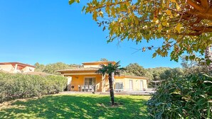 Une villa jaune, avec un toit recouvert de tuiles, entourée d’une pelouse bien entretenue et de diverses plantes.