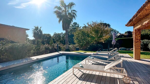 Une terrasse en bois avec une piscine, des chaises longues et une pergola.