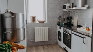 A modern kitchen with grey tiles, a window with a basket, a microwave, and a washing machine.
