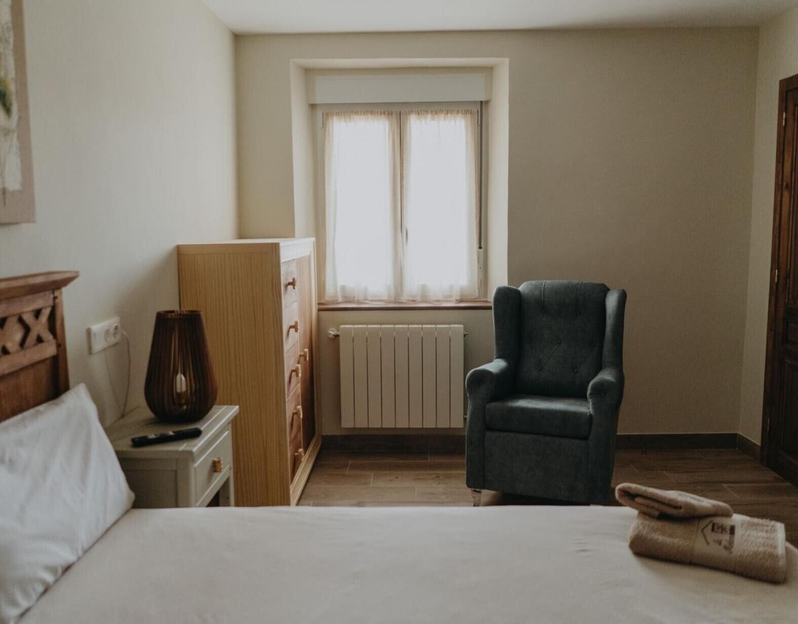A bedroom with a bed, a chair, a radiator, and a window.