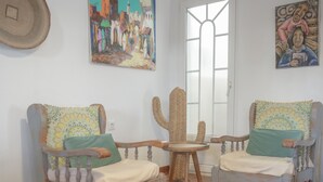 Una habitación con dos sillas de madera con cojines, una mesa tejida y dos cuadros en la pared.