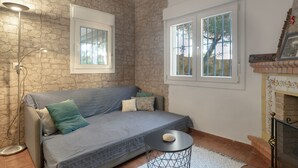 Una sala de estar con una pared de piedra, un sofá gris, una mesita redonda y una chimenea.