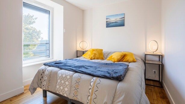 A bedroom with a bed, two bedside lamps, a window, and a wall-mounted picture. - Holiday Home 'Les Hirondelles' with Private Terrace, Private Garden and Wi-Fi (Mellac)