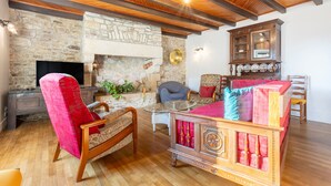 A cozy living room with a stone fireplace, wooden furniture, and a television. - Holiday Home 'Les Hirondelles' with Private Terrace, Private Garden and Wi-Fi (Mellac)
