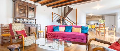 A spacious living area with a wooden ceiling, a glass coffee table, a red sofa, and a wooden cabinet.