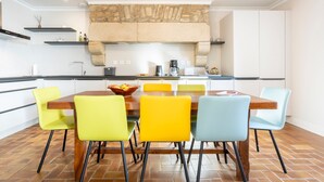 A modern kitchen with a stone fireplace, a dining table with six chairs, and a coffee maker. - Holiday Home 'Les Hirondelles' with Private Terrace, Private Garden and Wi-Fi (Mellac)