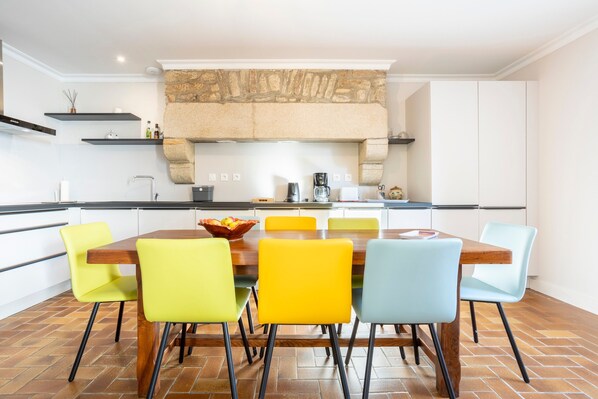 A modern kitchen with a stone fireplace, a dining table with six chairs, and a coffee maker.
