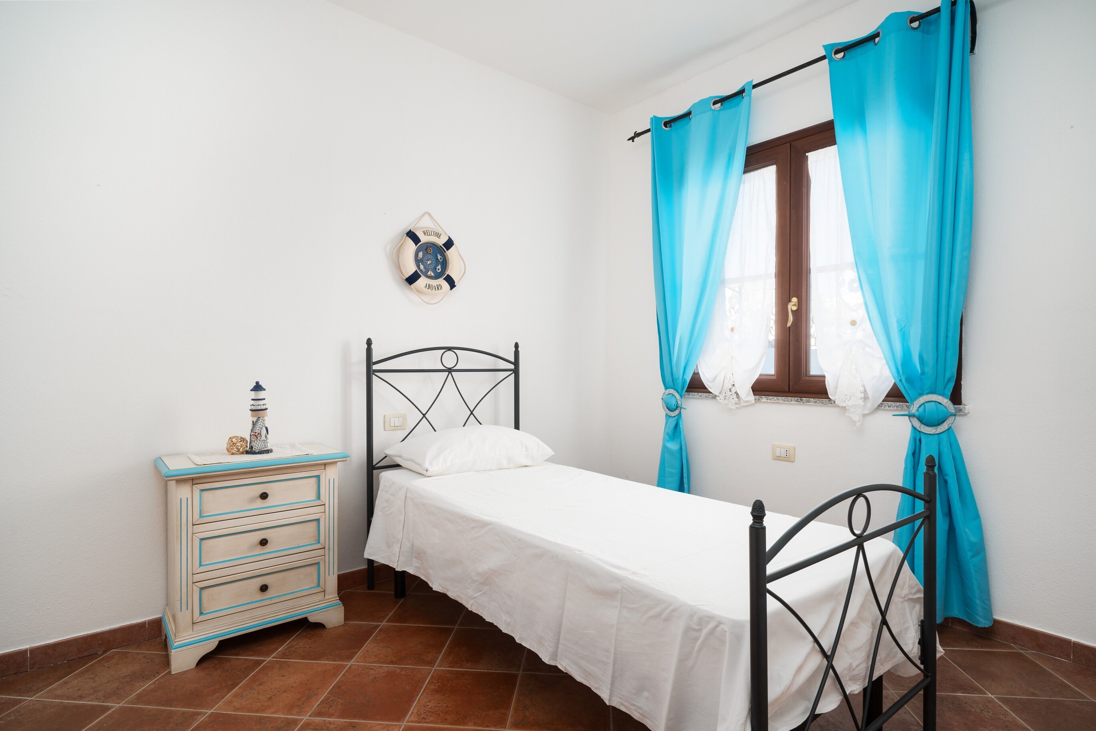 Een slaapkamer met een bed, nachtkastje, een klok aan de muur en een raam met gordijnen.