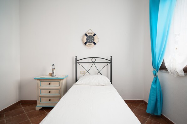 A single bed with a headboard, a bedside table with drawers, a wall clock, and a curtain.