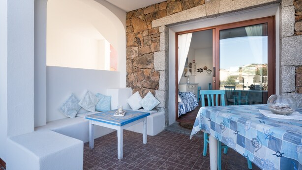 Ein Balkon mit Steinmauer, einer weißen Bank, einem Tisch mit blauer Tischdecke und Blick auf die Stadt.