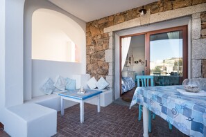 A balcony with a stone wall, a white bench, a table with a blue tablecloth, and a view of the city.