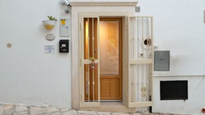 A white building with a wooden door, a small plant, and a mailbox on the wall.