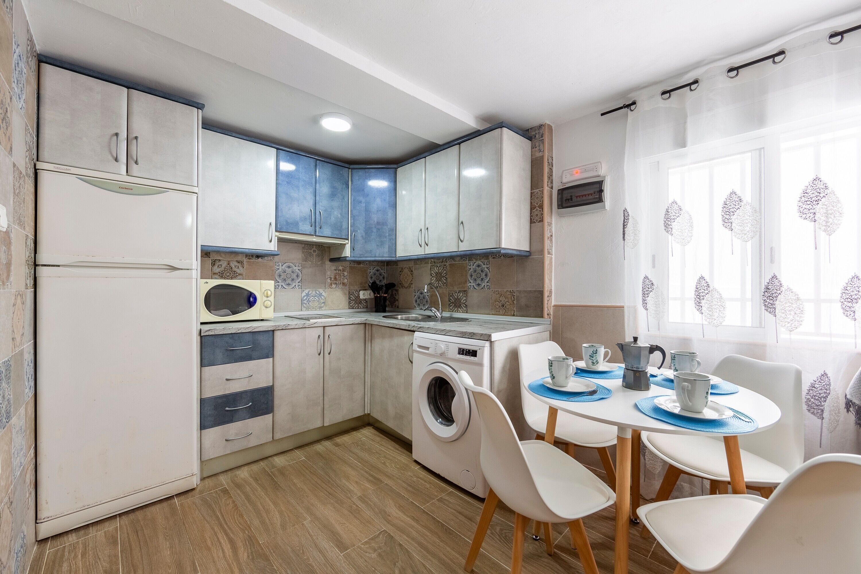 Una cucina compatta con lavatrice, forno a microonde e zona pranzo con sedie e tavolo.