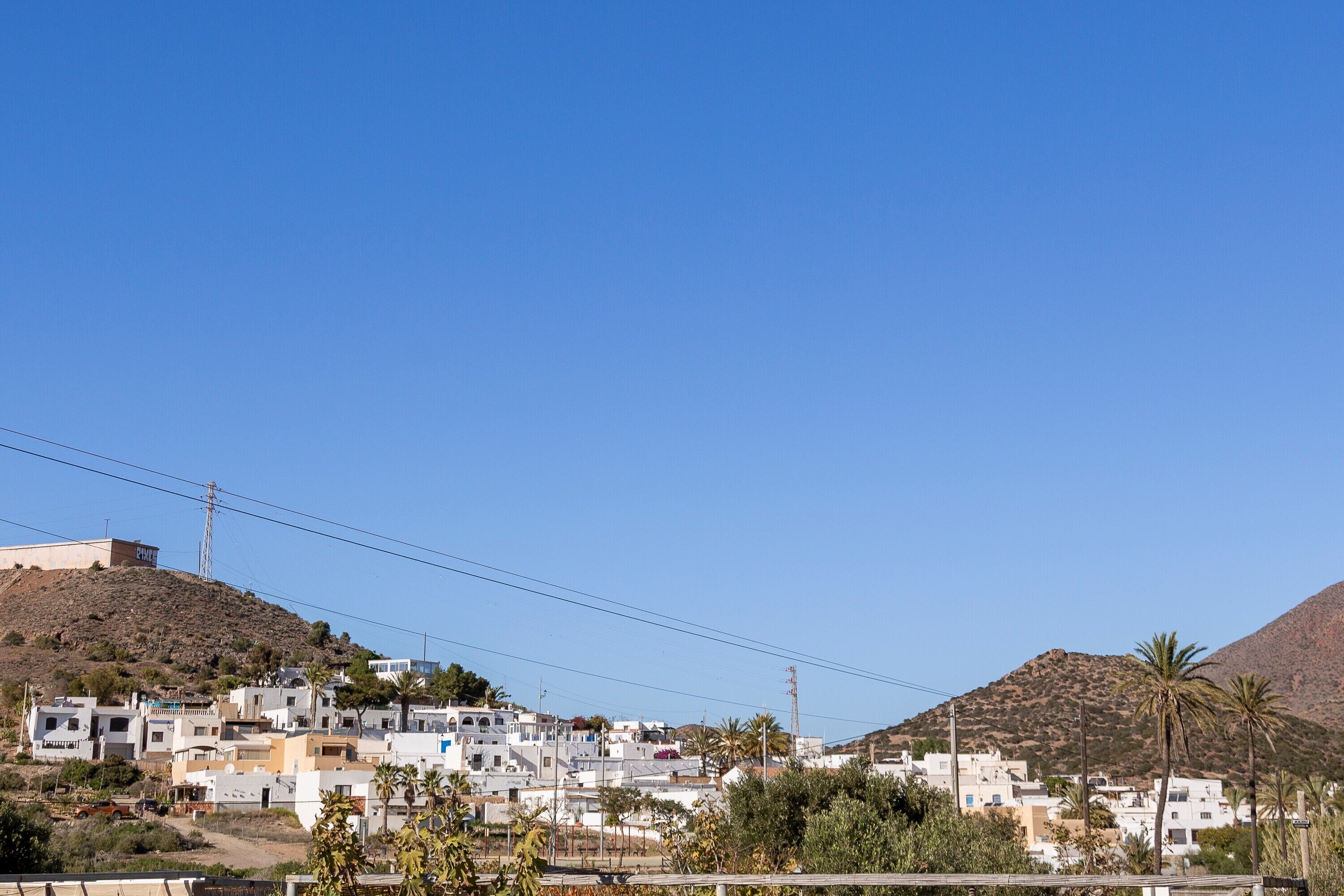 A hillside settlement with white buildings, some with blue doors, and palm trees.
