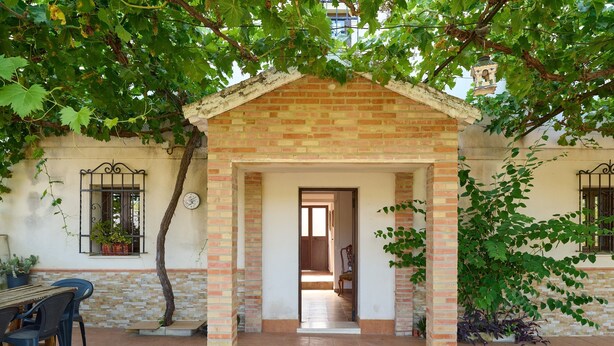 Un patio techado con una estructura de ladrillo, una mesa con sillas y plantas en macetas.