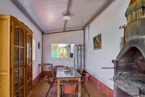 A dining area with a table, chairs, a wooden cabinet, a window, and a brick oven.