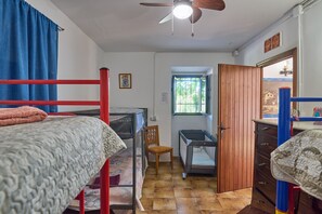 A room with bunk beds, a desk, a chair, a wooden wardrobe, a window, and a ceiling fan.