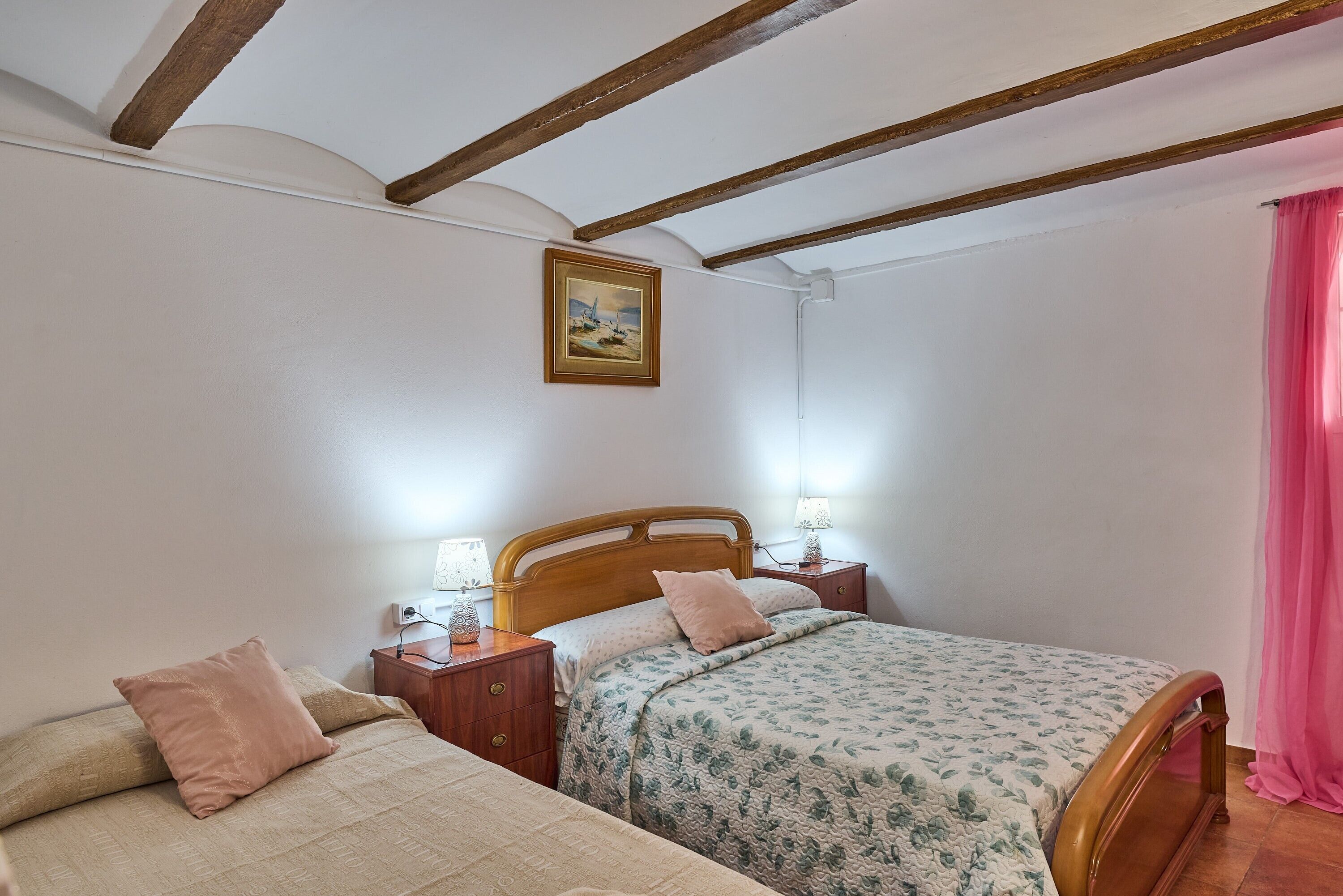 Een slaapkamer met een houten bed, twee nachtkastjes met lampen, een schilderij aan de muur en een roze gordijn.