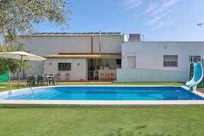 A swimming pool with a patio area, a slide, and a building with a tiled roof.