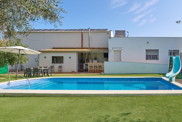 A swimming pool with a patio area, a slide, and a building with a tiled roof.