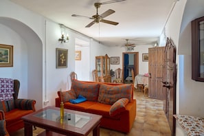 A living room with a sofa, chairs, a glass coffee table, ceiling fans, and a wooden cabinet.
