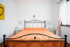 A bedroom with a metal bed frame, an orange bedspread, two bedside tables with lamps, and a wall decoration.