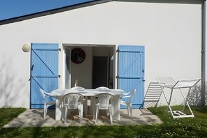 Edifici blanc amb persianes blaves, una taula amb caires i un rellotge a la paret.