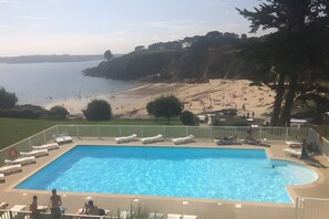 En swimmingpool med liggestole, udsigt til en strand og en græsplæne.