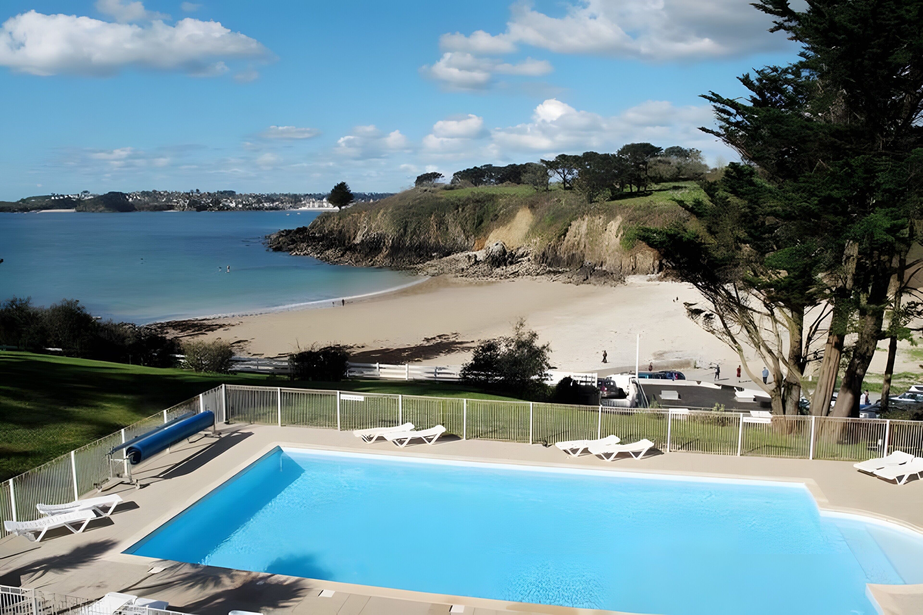 Una piscina con sillas de descanso, vista al mar y un área delimitada por una cerca.
