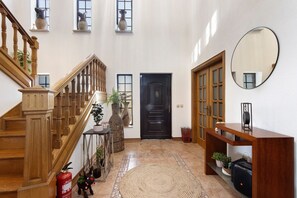 Ein geräumiges Foyer mit einer Holztretreppe, einer schwarzen Tür, einem runden Spiegel und einem Holzkonsolentisch.