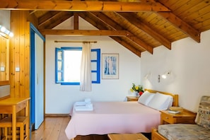 A room with a bed, a wooden desk, a window with blue shutters, and a ceiling with exposed beams.