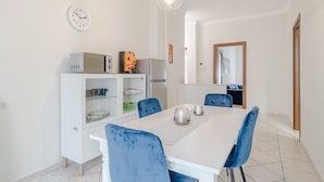 A dining area with a white table, blue chairs, a microwave, a refrigerator, and a clock on the wall. - GuestHost - Comfy APT in Santa Rita District (Torino)