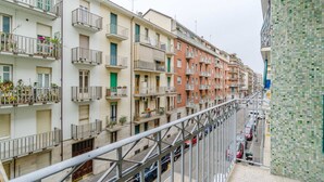 A row of multi-story residential buildings with balconies, a metal staircase, and parked cars on the street. - GuestHost - Comfy APT in Santa Rita District (Torino)