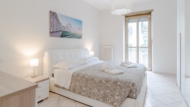 A bedroom with a bed, bedside table, lamp, and a painting on the wall. - GuestHost - Comfy APT in Santa Rita District (Torino)