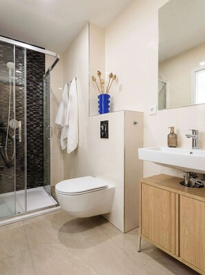 A modern bathroom with a glass shower enclosure, a white toilet, a sink with a wooden cabinet, and a mirror above the sink.