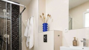 Ein modernes Badezimmer mit Duschkabine aus Glas, einer weißen Toilette, einem Waschbecken mit Holzschrank und einem Spiegel über dem Waschbecken.