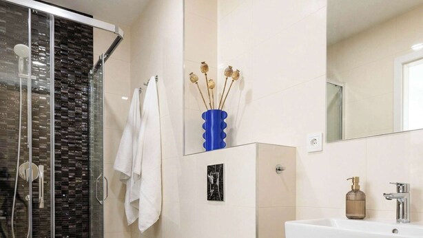 A modern bathroom with a glass shower enclosure, a white toilet, a sink with a wooden cabinet, and a mirror above the sink. - TurnKey | Wenceslas Square Loft Apartment IV (Praha 1)