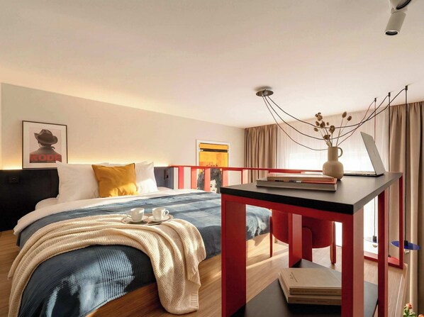 A modern hotel room with a bed, bedside table, and a desk with a laptop.