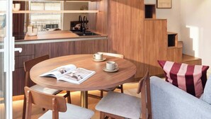 Un intérieur moderne avec une table de salle à manger ronde, des chaises en bois, un canapé et un coin cuisine doté d’un meuble intégré.