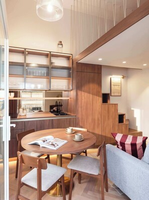 A modern interior with a round dining table, wooden chairs, a sofa, and a kitchen area with a built-in cabinet. - TurnKey | Wenceslas square Two Level Apartment XI (Praha 1)
