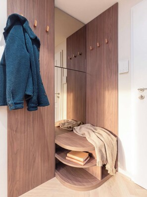 A room with a wardrobe, a bench with a blanket, and a coat hanging on the wall.