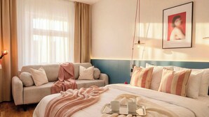 A hotel room with a bed, a sofa, a bedside table, a lamp, and a framed picture on the wall. - TurnKey | Wenceslas square Apartment II (Praha 1)