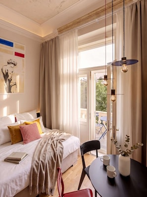 A well-lit bedroom with a bed, bedside table, and a view of the outdoors.