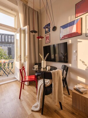 A modern living room with a dining area, a flat-screen TV, and a balcony with outdoor furniture.