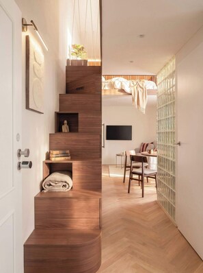 A modern interior with a wooden staircase, a dining area with a table and chairs, and a wall-mounted television.