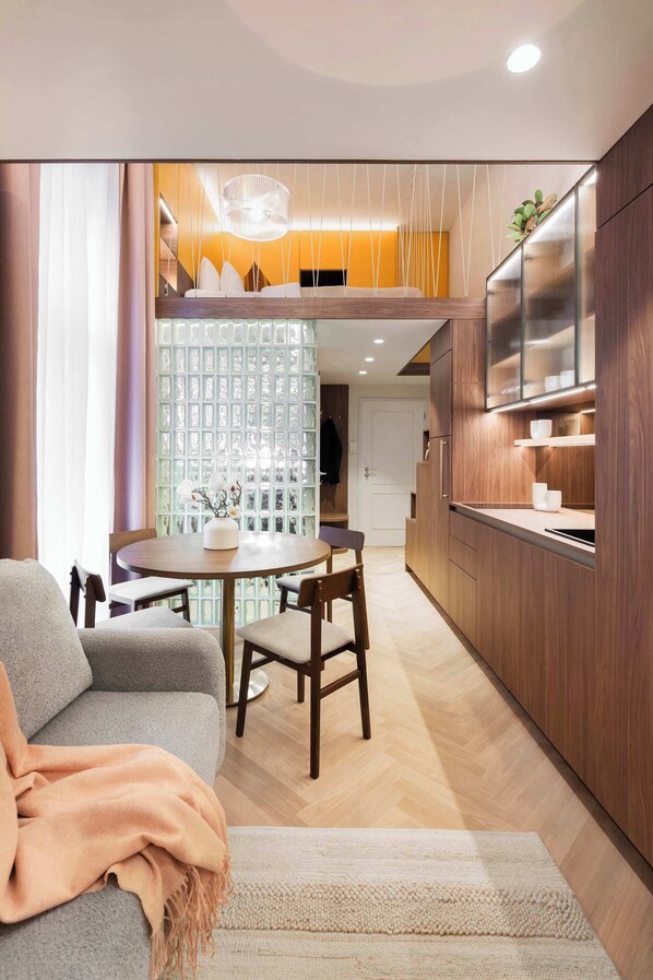 Une cuisine moderne avec des meubles en bois, un coin repas avec une table ronde et des chaises, et un espace salon confortable avec un canapé et un plaid.