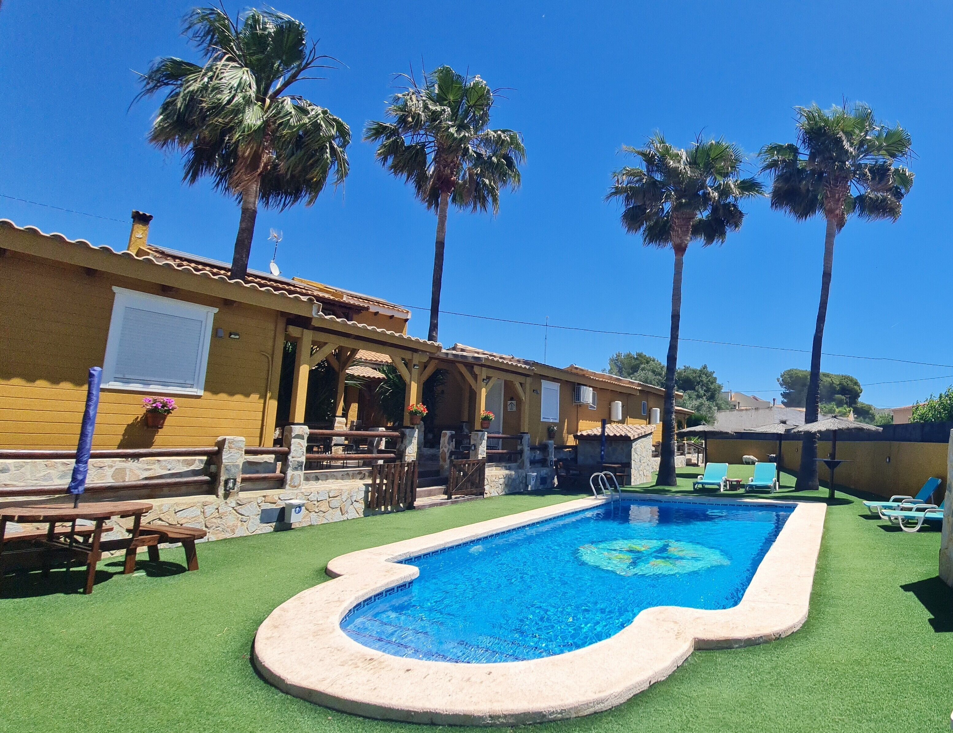 A pool with a unique shape, surrounded by palm trees and a building with a tiled roof.