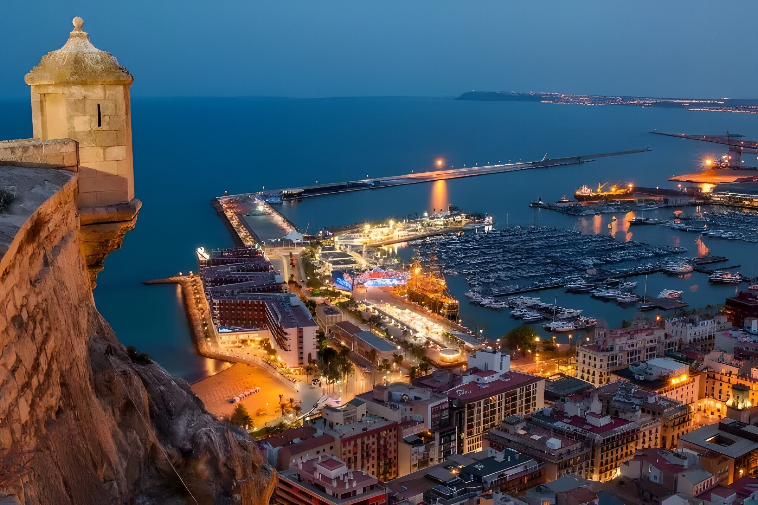 A coastal cityscape with a prominent tower, marina, and waterfront buildings.