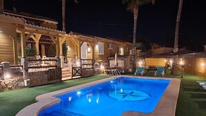 A swimming pool with a stone edge, surrounded by a covered patio area with outdoor seating.