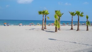 A beach with palm trees, umbrellas, and lounge chairs.